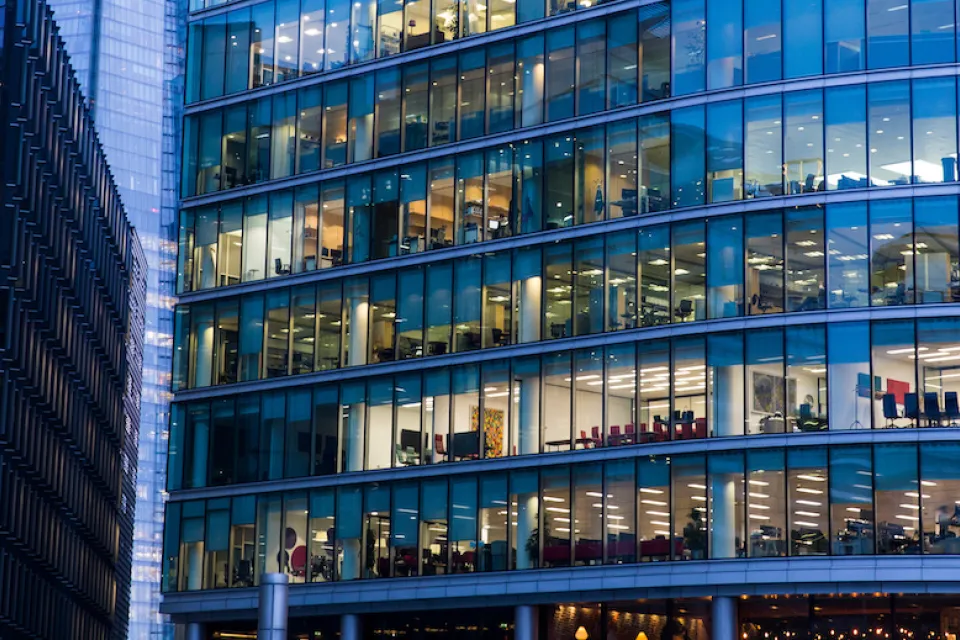 Close-up of glass facade of office building with office furniture visible through the windows.